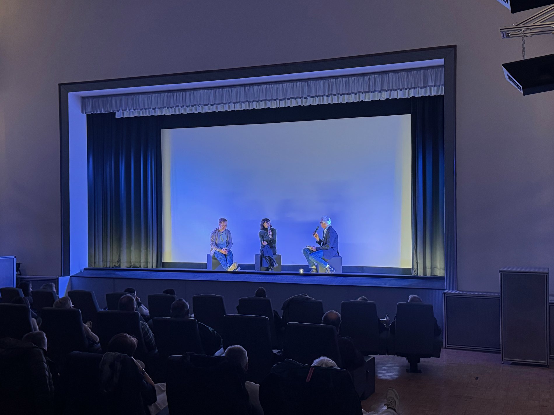 Blick in den Saal Ferdinand mit Publikum und beleuchteter Leinwand