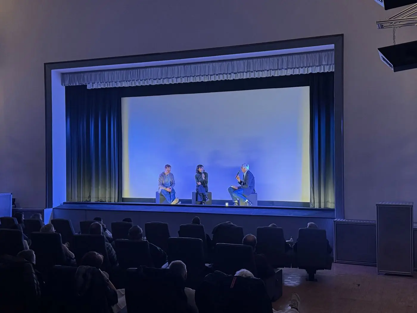 Blick in den Saal Ferdinand mit Publikum und beleuchteter Leinwand